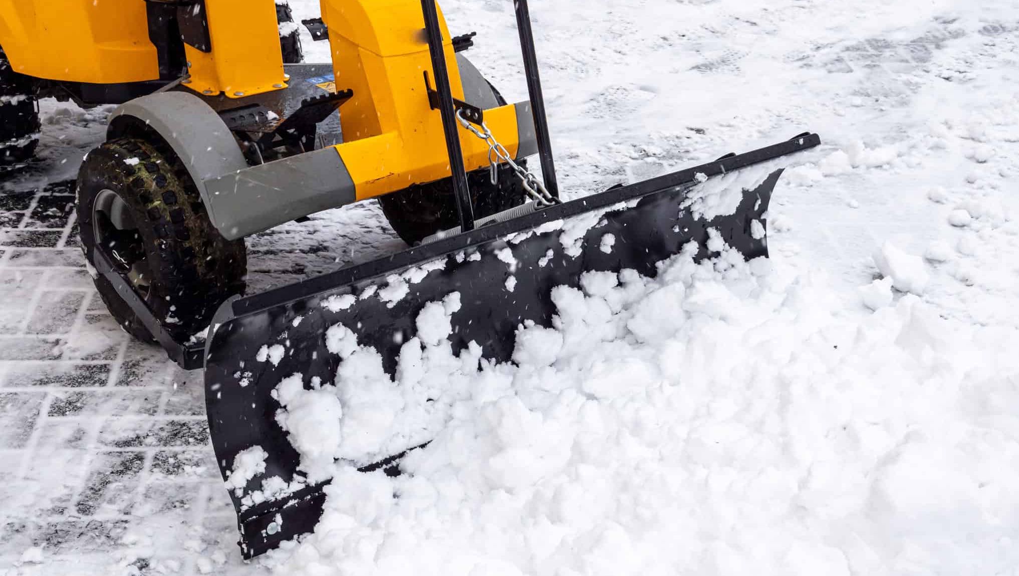 Snøfreser med plogblad rydder snø fra gangvei og uteområde i vinterlige omgivelser.